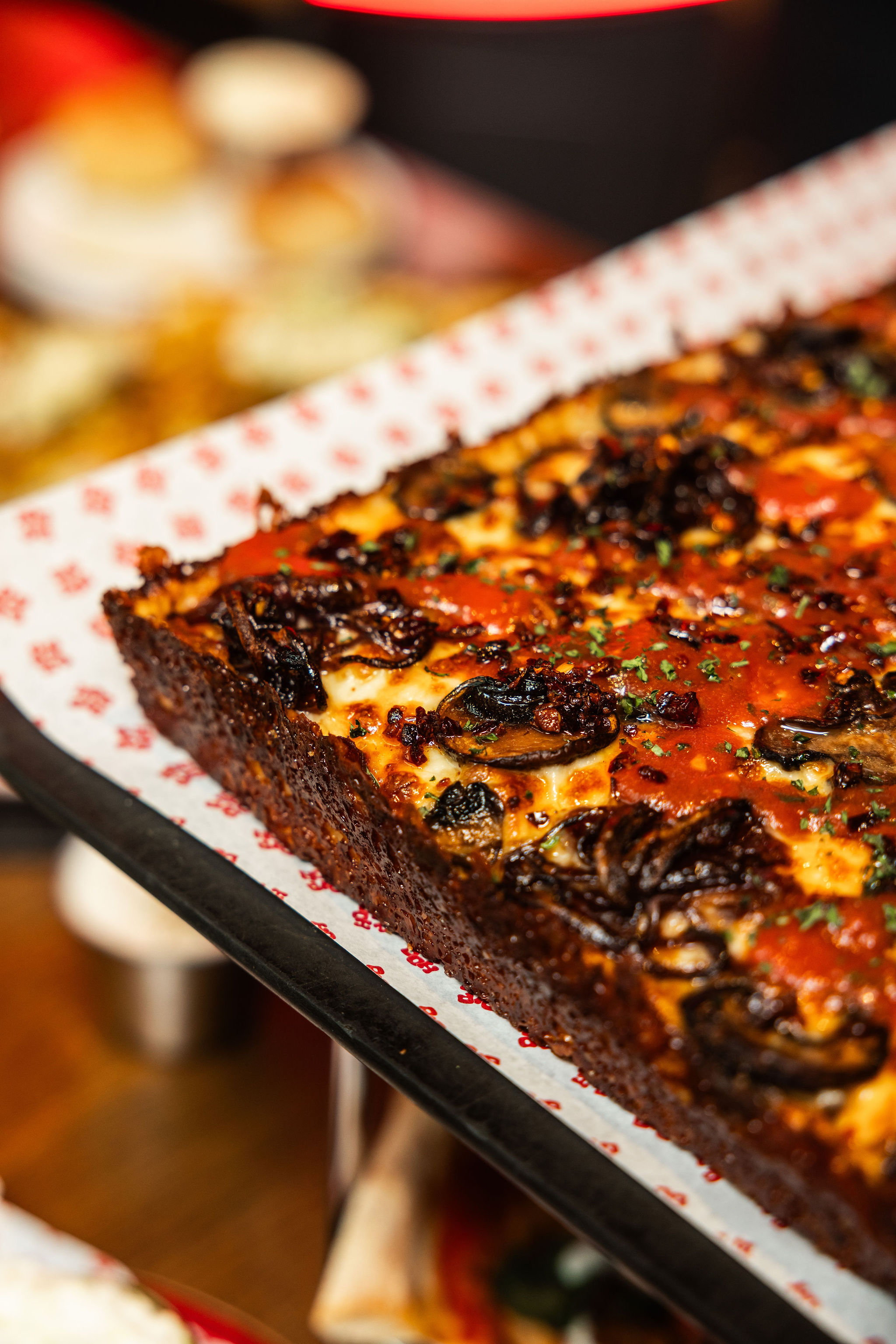 Close-up of a Detroit-style pizza topped with mushrooms, pepperoni and herbs.