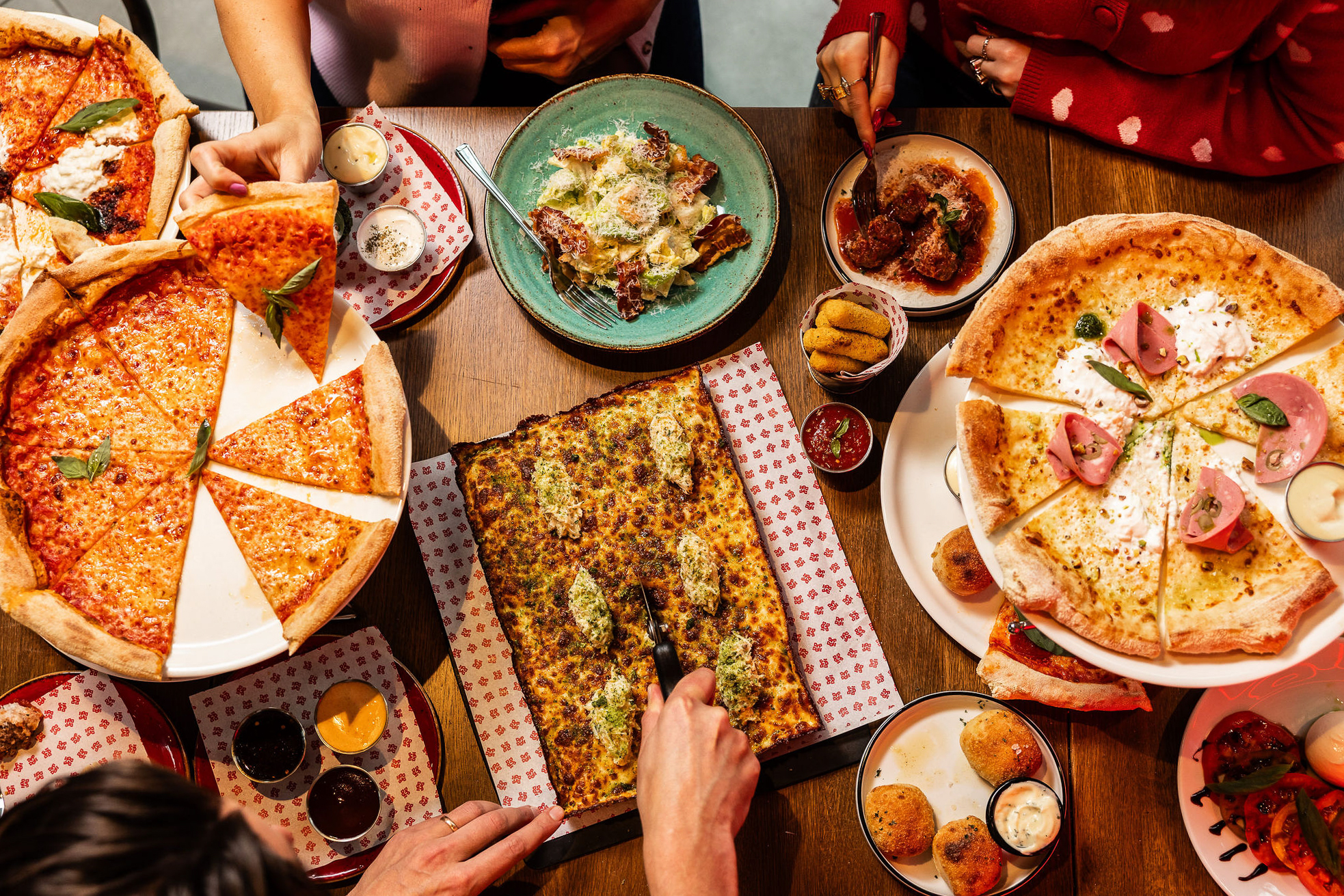 Overhead view of diners sharing round and Detroit-style pizzas, salads, sides and dips at Dip Doh Pizza Co.